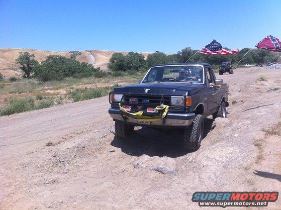 1990 Ford Bronco front view, dark blue, off-roading with flags
