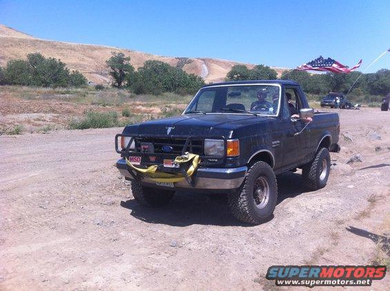 Black Ford F-150 pickup truck with aftermarket bumper and American flag flying