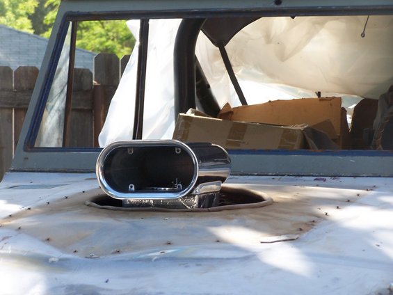 Chrome air scoop on a weathered vehicle hood, interior visible with covered items