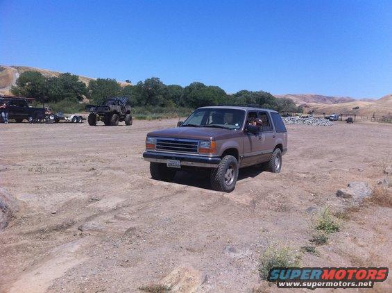 Brown 1990s Ford Explorer parked on dirt with other vehicles in background