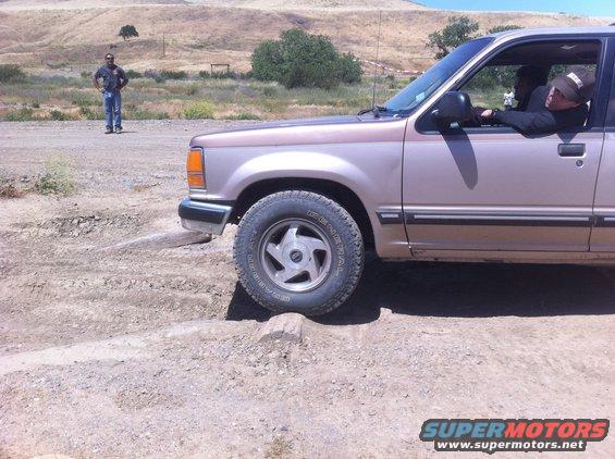 Tan Ford Explorer with a brown stripe, front wheel on a rock, driver looking out window