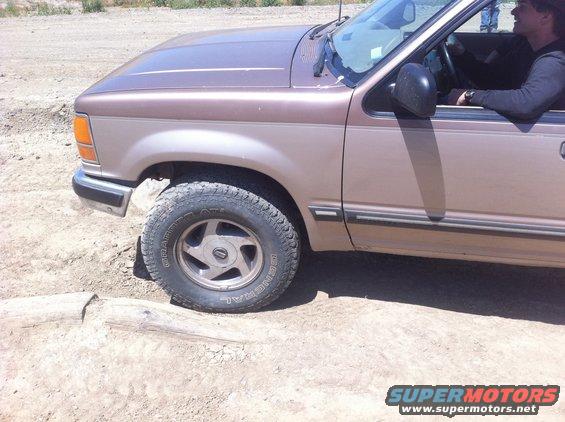 Front quarter view of a brown 1990s Ford Explorer driving on a dirt road