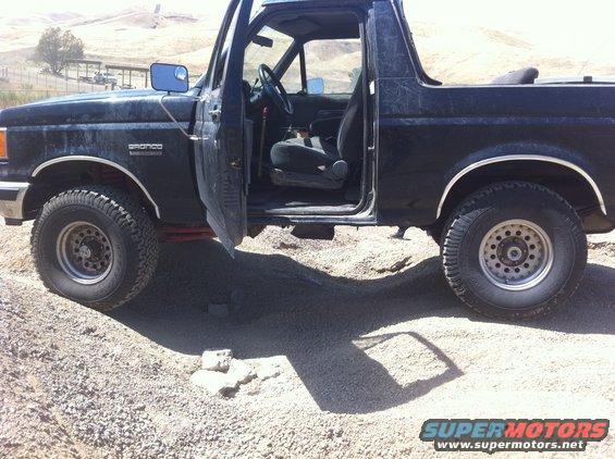 Black 1990 Ford Bronco with driver's door open, parked on gravel