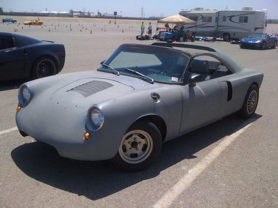 Gray custom sports car with a louvered hood and round headlights parked on asphalt
