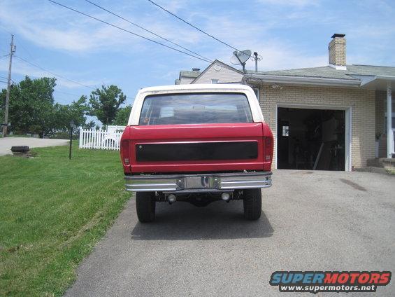 Red and white Ford Bronco parked in driveway, rear view. Chrome bumper, black panel on tailgate