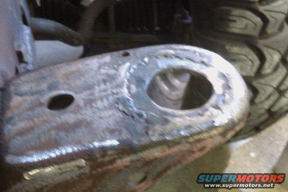 rusted metal bracket with a large circular opening and a smaller oval hole, possibly part of a suspension system