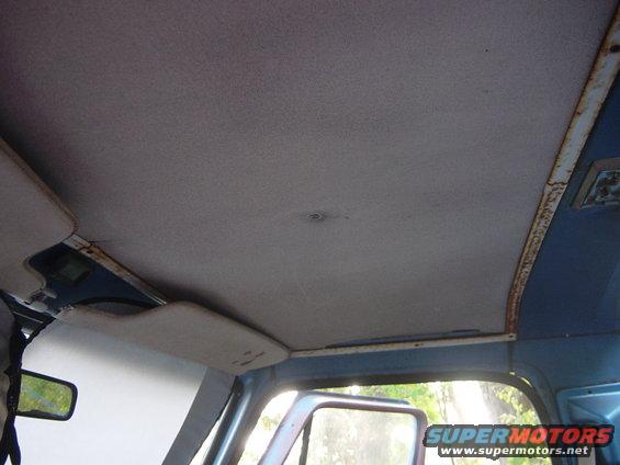 Vehicle interior showing a gray headliner, sun visor, and a reflection in the side mirror