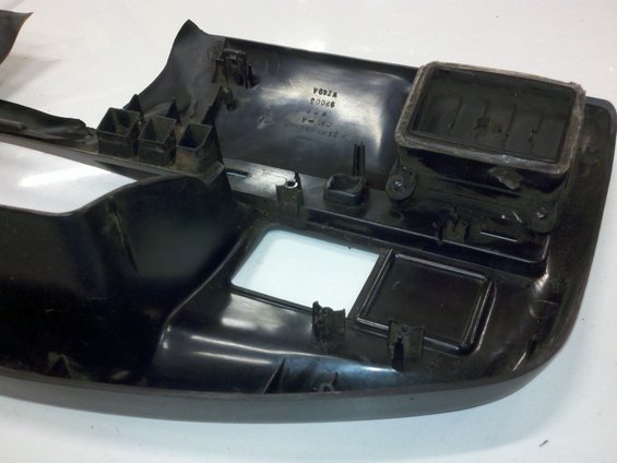 Black plastic dashboard trim with vents and cutouts, showing part numbers