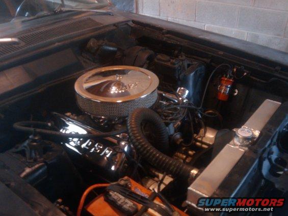 Engine bay with chrome air cleaner, V8 engine block, and aluminum radiator. Some wiring and a red ignition coil are visible