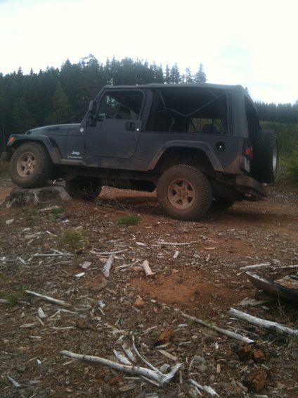 Dark blue 2005 Jeep Wrangler on a dirt path with trees in background
