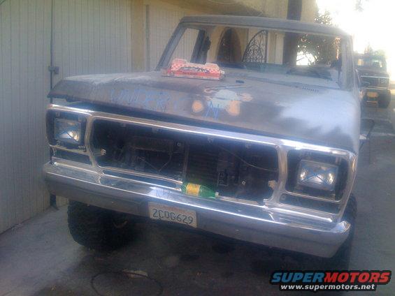 Primer-gray pickup truck front with chrome grille and license plate 2COG629. Another truck is visible behind