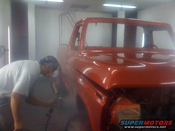 Man spray painting an orange 1978 Ford Bronco cab in a workshop