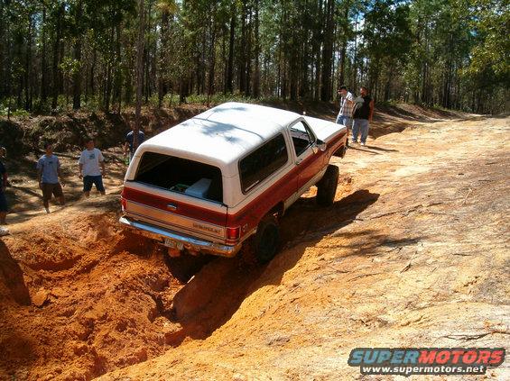 Red and white SUV with a white hardtop, driving off-road through a dirt rut