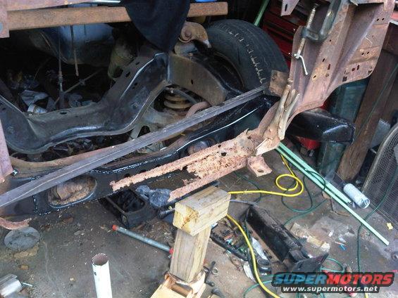 Rusty vehicle frame section with suspension components and a tire visible