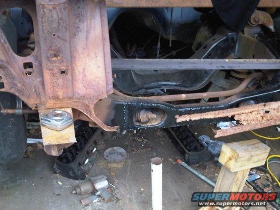 Underside of a vehicle with rusty frame rails, suspension parts, and an engine block on the ground