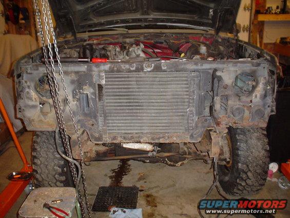 Front end of a Ford F-Series truck, hood up, radiator exposed, being worked on