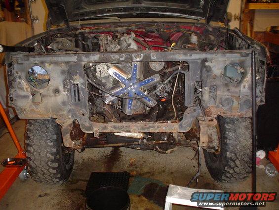 Front view of a disassembled 1980 Ford Bronco with engine exposed, showing rust and missing body panels
