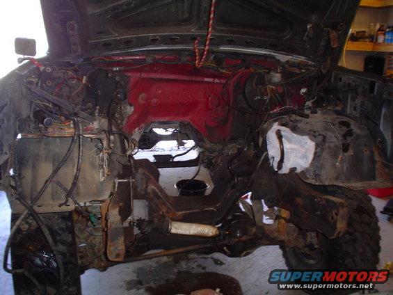 Vehicle engine bay with hood open, showing disassembled engine components and wiring