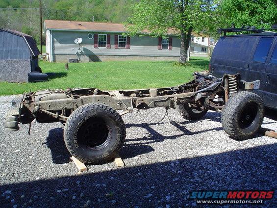 Truck chassis with large tires, front suspension visible, parked on gravel