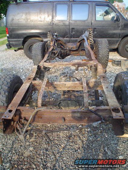 rusted frame of a vehicle, with a dark van behind it