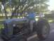 1983 Ford 427 - A man sits on a weathered tractor, which is parked outdoors on a paved surface.