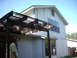 1983 Ford 427 - A man stands outside a house next to a wooden pergola on a sunny day.