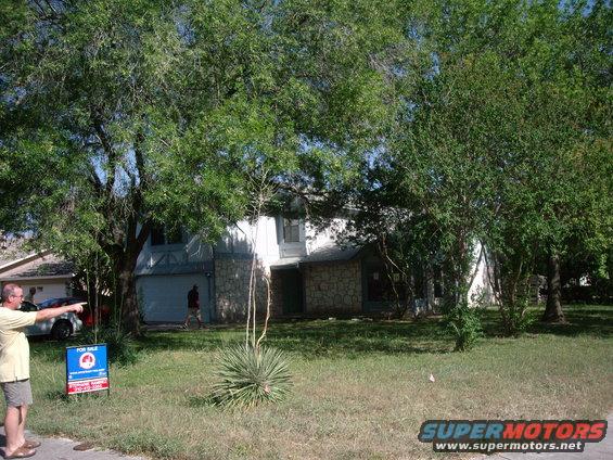 Man points at a house with a "For Sale" sign in the yard