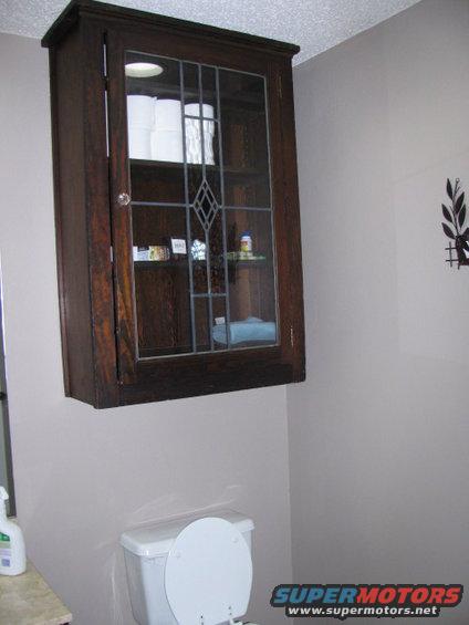 Wooden bathroom cabinet with glass door above a toilet