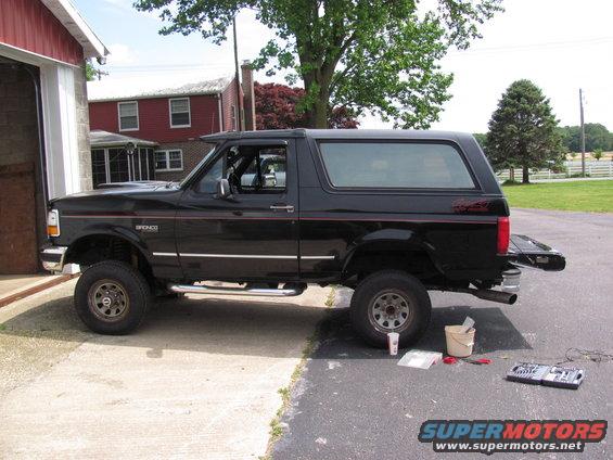 black Ford Bronco parked outside a garage, tailgate open, tools on the ground