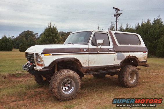 White and brown 1978 Ford Bronco lifted with large tires, parked in a grassy field