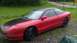 1993 Ford Probe - A red 1993 Ford Probe coupe with a black hood and roof is parked outdoors on a gravel and grass surface.