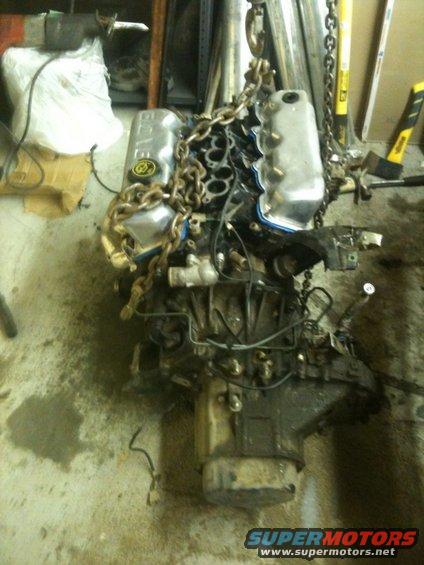 Engine assembly suspended by chains, with "SUPERMOTORS" logo visible at bottom right