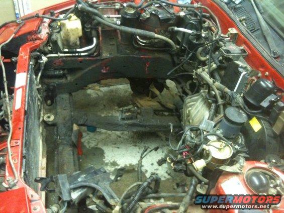 Red car engine bay with engine removed, showing exposed frame and wiring