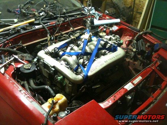 Red car engine bay with engine being lifted by straps. Visible text: '24 VALVE DOHC'