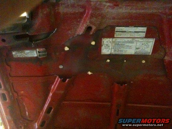 underside of red car hood with stickers and some damage