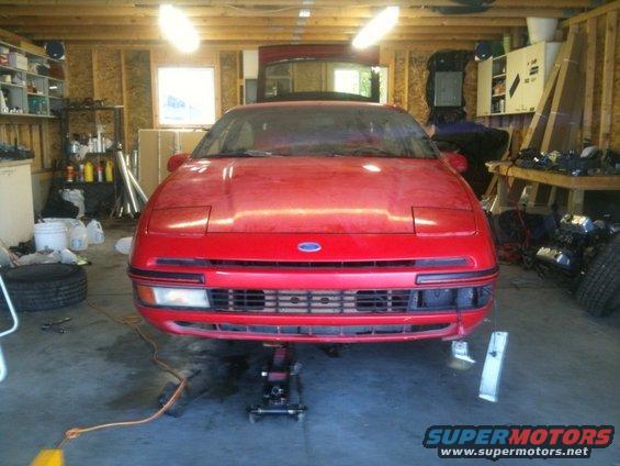 Red 1990 Ford Probe on a jack in a garage, front view