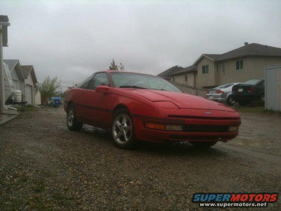 Red 1990 Ford Probe parked in a gravel driveway with houses and garages in the background