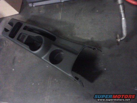 Black plastic center console with two cup holders and vent, lying on a dark surface