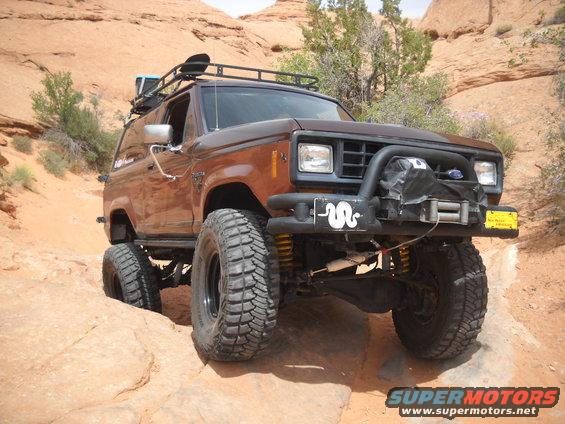 1986 Ford Bronco II with roof rack and winch, driving on rocks