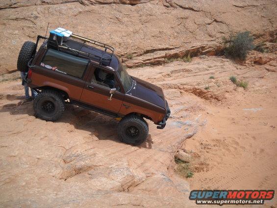 Brown Ford Bronco II with off-road tires and roof rack on rocky terrain