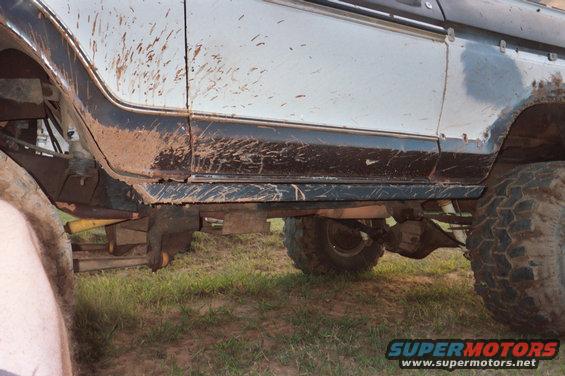 Mud-splattered side of an off-road vehicle showing rock skids and suspension