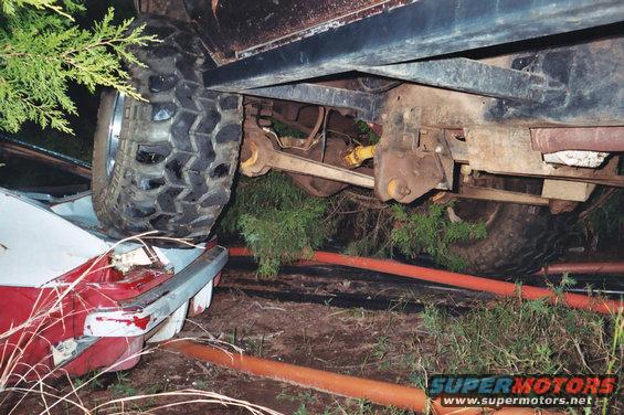 Undercarriage of a lifted off-road vehicle, tire on a white car. Orange pipes on ground
