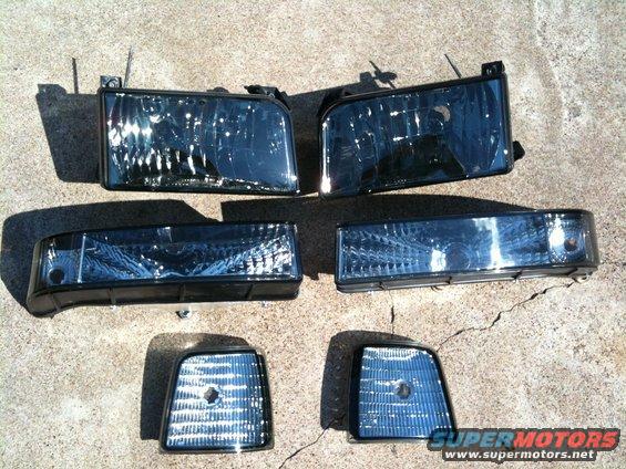 Four aftermarket headlights and corner lights for a vehicle, laid out on concrete