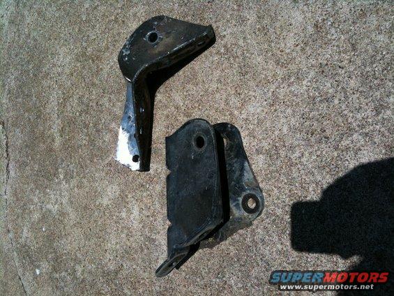 Two black metal brackets on concrete. Text reads SUPERMOTORS.NET