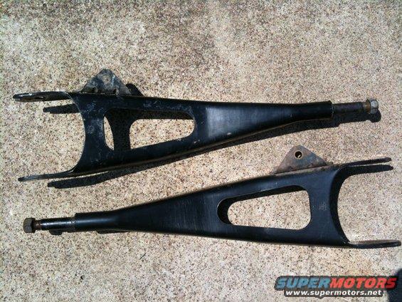 Pair of black control arms on concrete. Supermotors.net logo visible