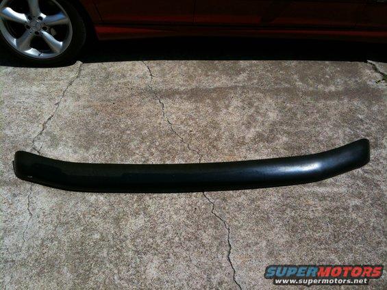 black plastic trim piece on concrete, red car wheel in background