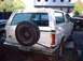 1978 Ford Bronco - Rear view of a white 1978 Ford Bronco, showing its spare tire mount and a dark truck in the background.