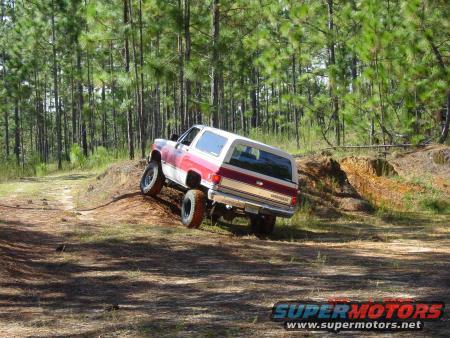 Red and white SUV with lifted suspension driving on a dirt hill in a forest