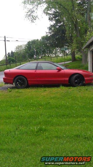 Red 1993 Ford Probe coupe with black roof and black wheels parked on grass