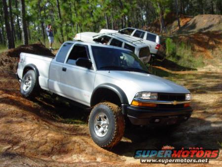 White pickup truck with off-road tires on a dirt track, two SUVs behind it